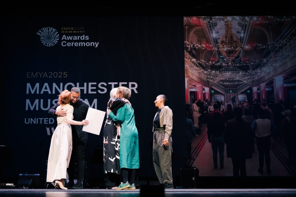 Manchester Museum team members embrace the judges and hosts on stage at the European Museum of the Year Awards after winning the main prize.